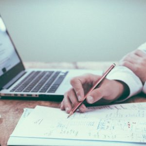two people writing on paper with laptops
